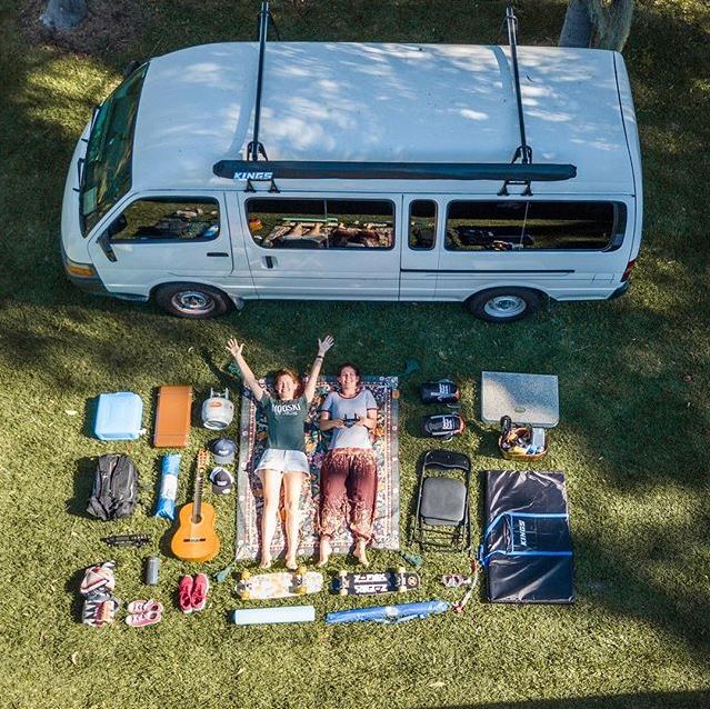 two women laying on a rug on grass in front of a campervan with items around them