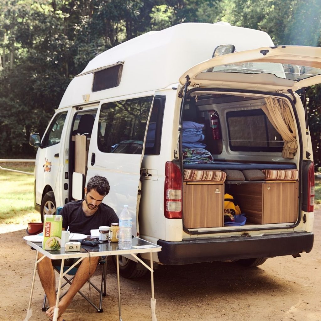 Man sitting by a small table outside of a campervan