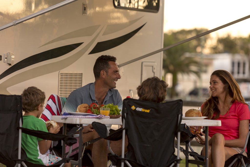 man, woman and back of young boy sitting around a table outside a motorhome