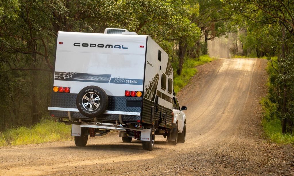 rear view of a 4x4 towing a Coromal Thrill Seeker caravan on a dirt road with trees in the background