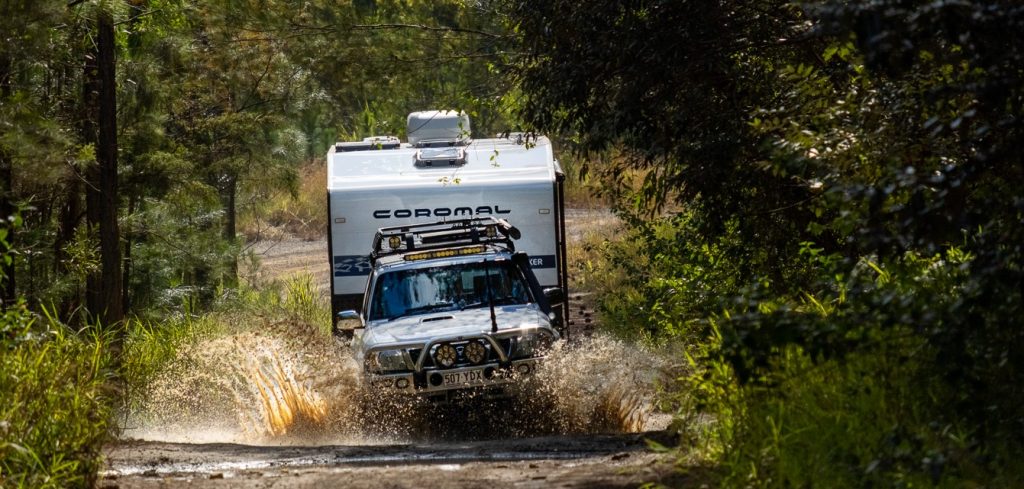 4x4 towing a Coromal Thrill Seeker caravan through a shallow river amongst trees